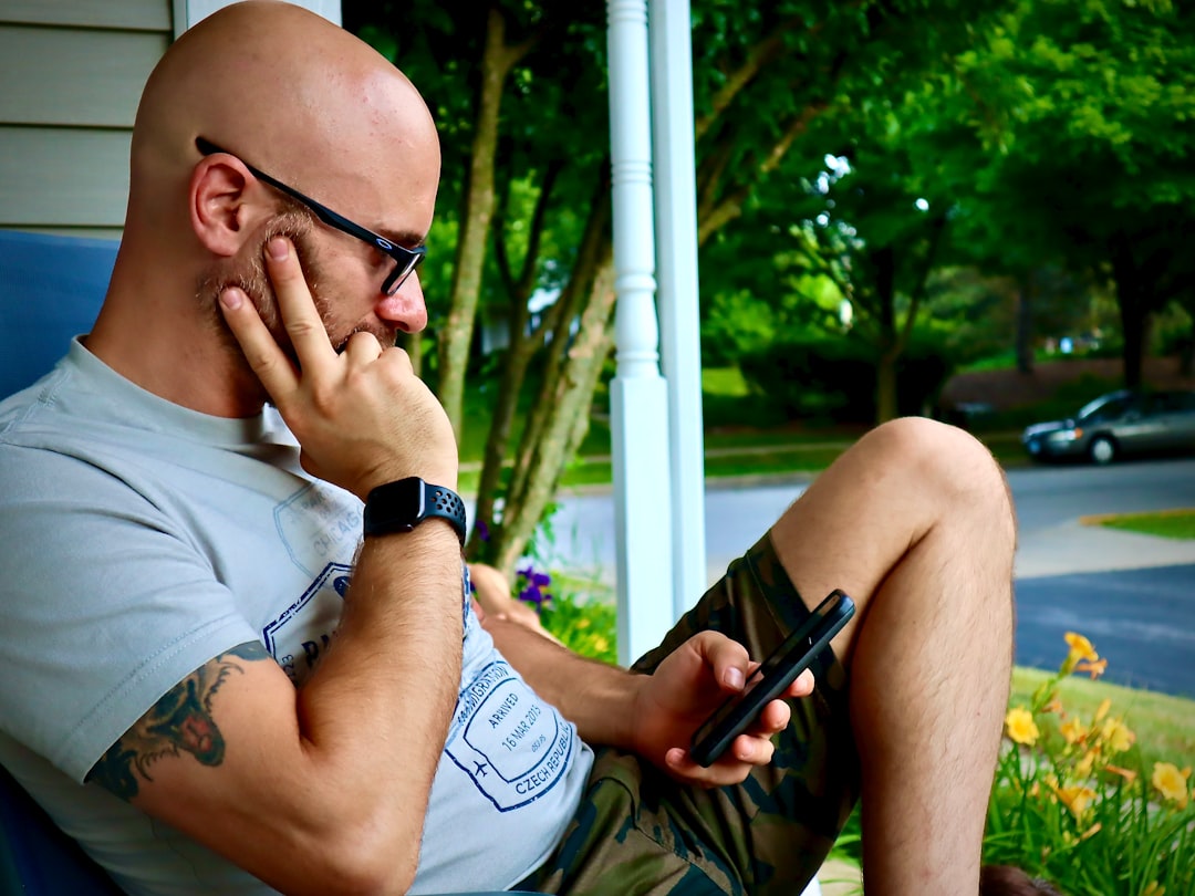 man in white tank top wearing black framed eyeglasses holding black smartphone