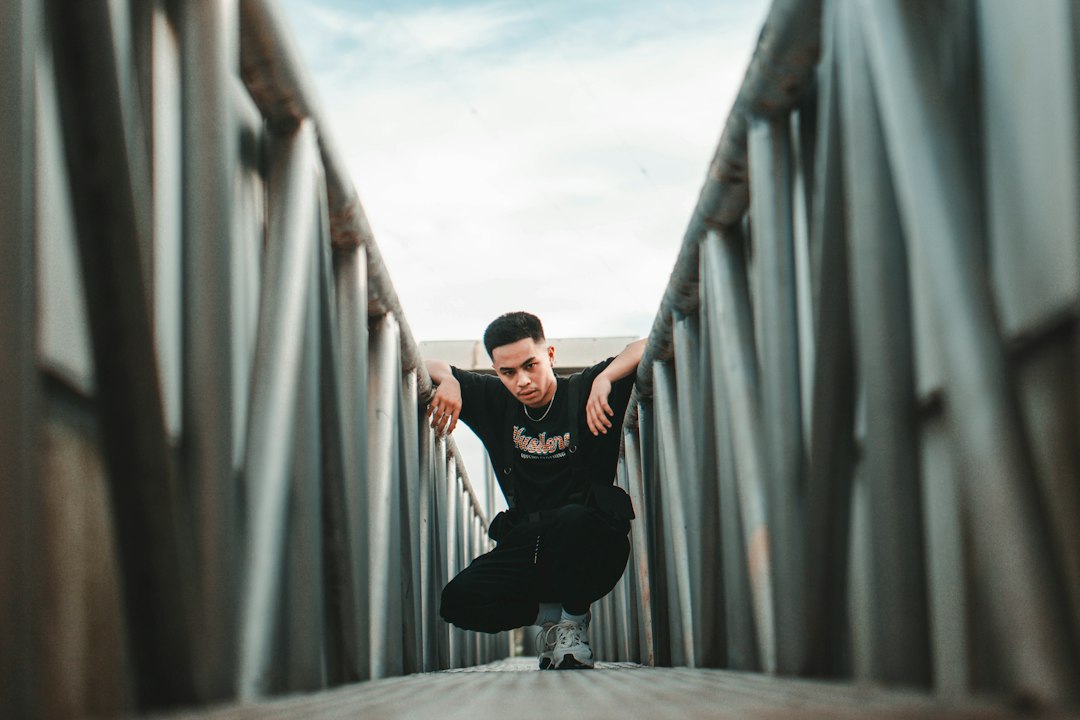 man in black t-shirt and black pants sitting on gray metal railings during daytime