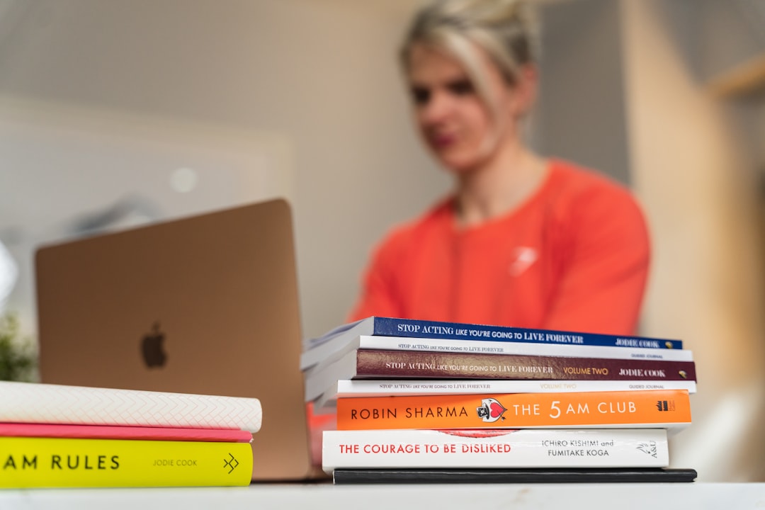 a woman sitting at a table with a stack of books in front of her
