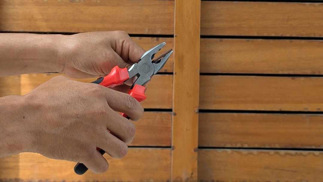Hands holding red and black pliers gripping a small metal rod